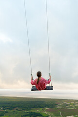 Little girl is on a swing under cloudy sky. Montana Redonda - obrazy, fototapety, plakaty