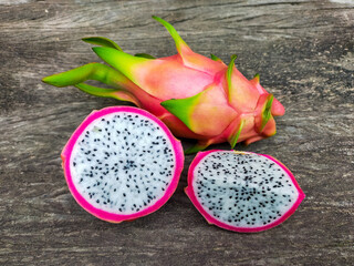 Juicy pink dragon fruit with white flesh and black seeds lying on old wooden background.