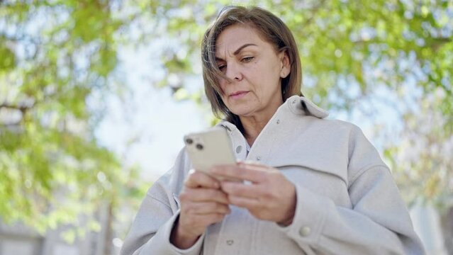 Middle age hispanic woman using smartphone at park
