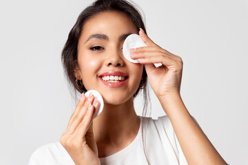 Modern asian woman removing makeup from face using cotton pads, apply cleansing cosmetics products...
