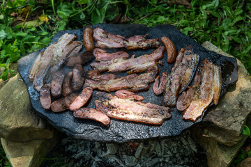 Preparing the barbecue on a special black stone base that can be covered with wood and firewood from below. Grilling homemade bacon and homemade sausages. A specialty from Serbia.