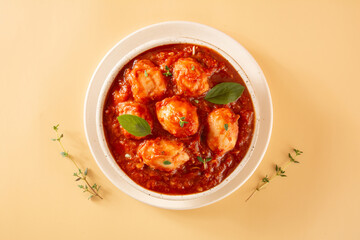 Delicious Gnocchi with Red Sauce and Basil served in a White textured Handmade Ceramic Bowl in a beige clean background with thyme decoration in top view