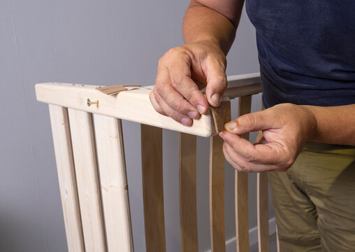 A man glues a rug on a wooden leg of the bed, a floor mat to the wooden legs of the bed. Men's hands install a square anti-slip felt pad on the wooden leg of the furniture.