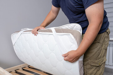 A man fastens a mattress topper to a mattress.