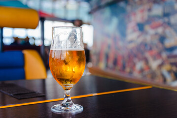 A beer in Tulip glass. Glass of light beer on wooden table in cafe or restaurant .Beautiful crystal glass with golden freshly brewed cold wheat beer stands on table cafe,restaurant terrace.