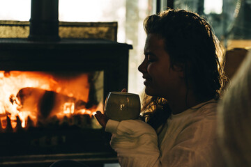 Woman in sweater has rest near the fireplace.