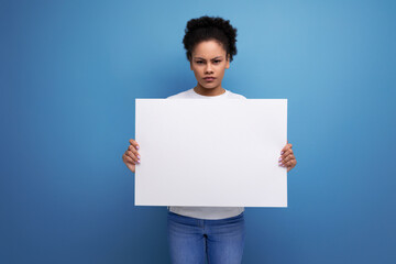 young brunette woman with afro hair in a white tank top holding a white board sheet with space for information