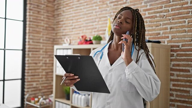 African american woman doctor reading medical report talking on smartphone at the clinic