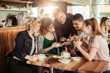 Diverse group of young people using a smart phone while having coffee at a cafe