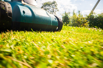 Lawn mower in motion on green grass in garden or backyard. Machine for cutting lawns. Gardening care tools and equipment. Process of lawn trimming