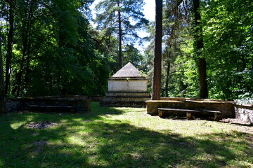 A view of an old abandoned war cemetery with a stone and marble mausoleum, several wooden crosses and stone tombs scattered all over a well maintained lawn and some paths in Poland seen in summer