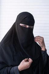 Muslim woman in black Nigab or Hijab in white wall, businesswoman wears Nigab or Hijab traditional cloth, looking at camera