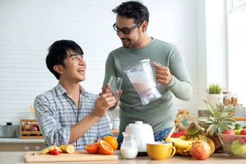 LGBTQ couple making various fruit healthy smoothies for breakfast in their kitchen at home, pouring smoothie to glass, healthy food concept