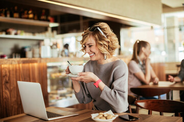 Young woman using a laptop in a cafe while having a cup of coffee
