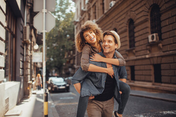 Fototapeta premium Young man carrying his girlfriend on a city street while they are traveling on their vacation