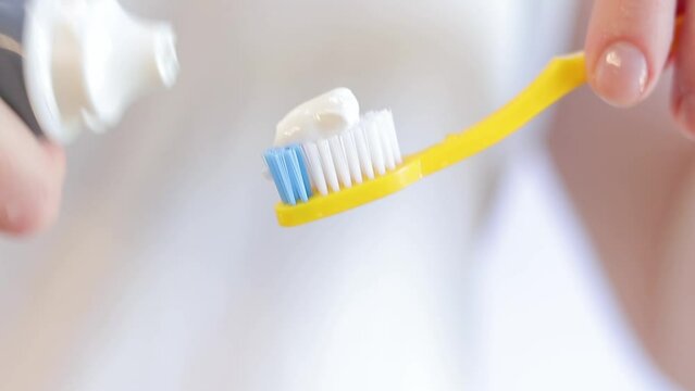 Squeezing out toothpaste on a yellow toothbrush, close-up. Brush your teeth. Health care, dental hygiene. A woman in the bathroom is squeezing white toothpaste out of a tube