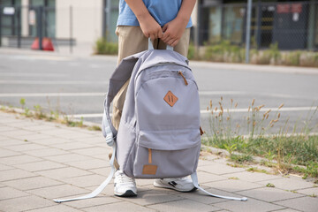 the boy is holding a gray backpack. A warm autumn day. Back to school. Close-up of children's legs,...