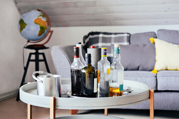 Alcohol bottles, metal cup on a low table at home. Cozy couch, pillows, globe on the background
