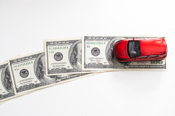 A close-up model of a beautiful sports car stands on a 100 American dollar bill isolated on a white...
