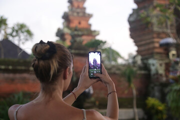 Tourist woman taking photo of Balinese temple with phone