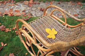 A yellow maple leaf is lying in a rocking chair in the autumn garden. Soft focus. Autumn postcard