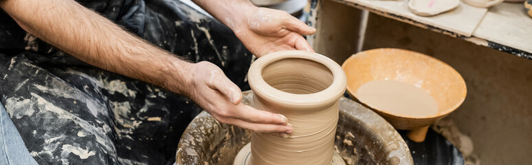 banner, Cropped view of sculptor shaping clay on pottery wheel in ceramic studio at background