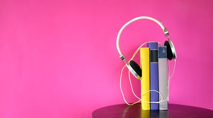Tuinposter audio book concept with stack of books and vintage headphones on pink  background,good copy space, panoramic © Kirsten Hinte