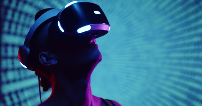Cyber gamer in VR glasses plays virtual reality game in neon futuristic space. Cyberpunk fashion gaming concept. Young handsome man looks around and shooting from virtual blaster gun.