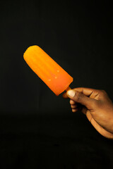 Orange ice cream in hand on a black background, closeup of photo
