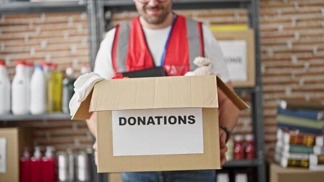 Grey-haired man volunteer wearing vest holding donations package at charity center