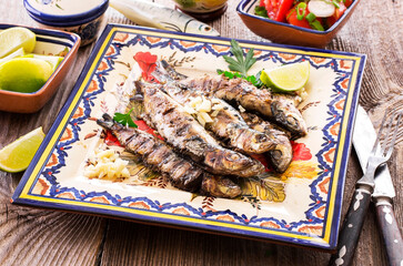 Traditional portuguese barbecue sardines with tomato salad and lemon slices served as close-up on a...