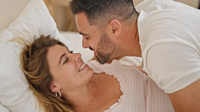 Man and woman couple lying on bed together kissing at bedroom