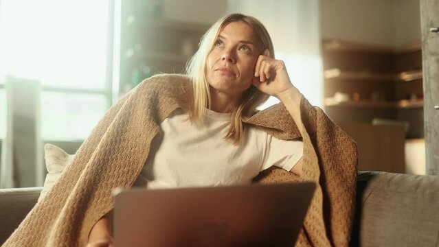 Sad blond mature woman or freelancer with lack of new ideas or creative block typing and deleting text on laptop computer at home Worried female changing her mind every few seconds indoors