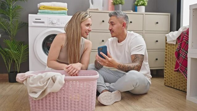 Man and woman couple washing clothes using smartphone at laundry room
