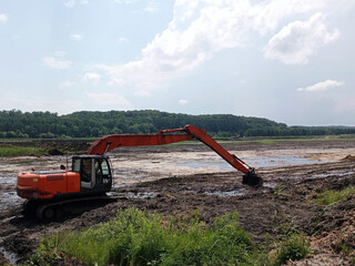 An orange excavator is working to clean the bottom of the pond, Excavator with a long arm. Heavy...