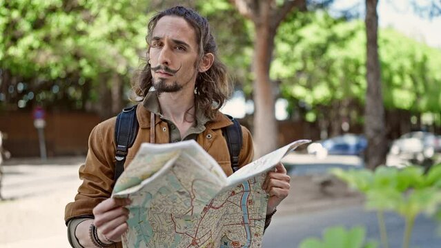 Young hispanic man tourist wearing backpack looking city map at park