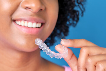 close up of african american girl smiling with transparent dental aligner in hand on blue background