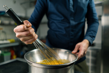 a chef in a professional kitchen whips the ingredients with a whisk for making craft author's ice cream close-up