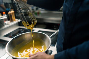 a chef in a professional kitchen whips the ingredients with a whisk for making craft author's ice...