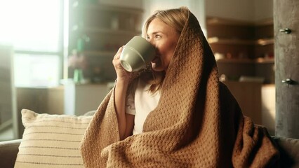Portrait of charming blond mature woman under the blanket take sip drinking hot tea or coffee sitting on couch at home Calm relaxed female enjoying weekend leisure time alone indoors - Powered by Adobe