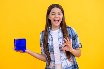 winking teen girl holding shopping box with present isolated on yellow background
