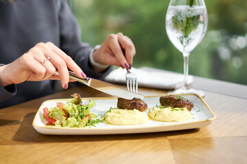 Lunch in a restaurant, a woman eats Delicious juicy meat cutlets, mashed potatoes sprinkled with greens and fresh healthy salad of tomatoes and lettuce leaves.