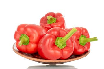Several red bell peppers on a clay plate, macro, isolated on white background.
