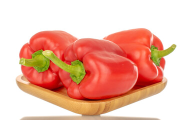 Three red bell peppers on a bamboo tray, macro, isolated on white background.