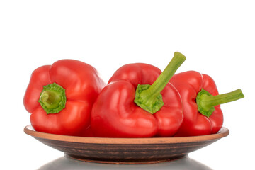 Three red bell peppers on a clay plate, macro, isolated on white background.
