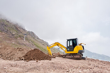 Obraz premium Excavator works in the highlands. Makes a trench for communications. water and electricity. in the gorge of the mountains. repair and expansion of a road