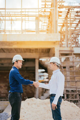 A full-body portrait of two Asian male engineers shaking hands and working together. Standing in the architectural construction site about the structural industry Wear a helmet