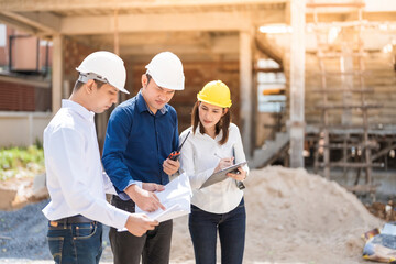 A team of 3 Asian male and female engineers are mechanics looking at architectural construction drawings in structural design. industrial Wears a helmet, has a radio and a listnote, a blueprint.