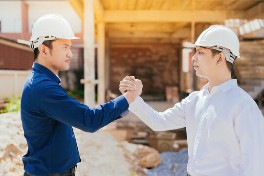 Close-up of two Asian male engineers hand in hand and working together. looking at each other with hope Standing in the architectural construction site about the structural industry wear a helmet