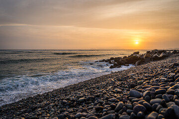 Sunset on the Pacific Ocean in Lima reflected on the stones of the beach - 628605253